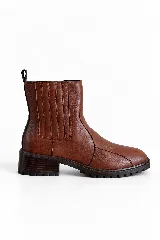 Botin de cuero vacuno color marrón, con taco bajo y suela track. Presenta una franja vertical negra en la parte trasera y cierre lateral.