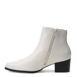 Bota de caña baja marca Bottero, confeccionada en cuero color marfil. Presenta un diseño minimalista con panel elástico lateral, punta redondeada y taco cuadrado en contraste de color negro.