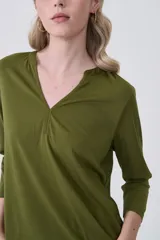 Remera de poliéster color verde oliva, con mangas 3/4, cuello en V con detalle de pliegue central y corte holgado.