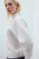 Camisa amplia blanca de cuello alto y manga larga, con cierre frontal de botones.