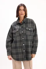 Camisa de corte oversize con estampado a cuadros en tonos verdes y grises, confeccionada en tela tipo franela. Presenta cuello clásico, cierre frontal con botones metálicos y dos bolsillos delanteros con solapa.