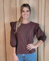 Remera de algodón color marrón chocolate, con cuello redondo y mangas tres cuartos abullonadas con detalle de volados en los hombros y puños elásticos.