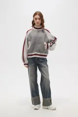Campera de punto con cierre frontal, cuello alto y diseño de rayas laterales en mangas. Presenta un patrón texturizado en el cuerpo y detalles de rib acanalado en puños, cuello y ruedo.
