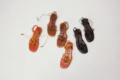 Sandalias planas de cuero color marrón, con diseño de punta cuadrada, tiras finas cruzadas y un detalle trenzado circular en el empeine. Cuentan con tiras para atar al tobillo decoradas con cuentas turquesas en las puntas.
