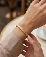Pulsera tipo esclava rígida de acero con baño de oro, con diseño estriado y detalles de incrustaciones de circonia.