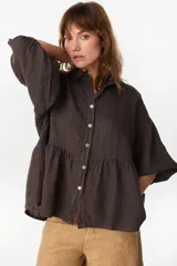 Camisa de lino marrón oscuro con silueta holgada, cuello camisero, cierre frontal de botones claros, mangas voluminosas y detalle de frunces en la cintura.