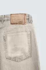 Pantalón de corte relajado confeccionado en tejido de algodón con efecto lavado. Presenta diseño de cinco bolsillos, cierre frontal con cremallera y botón, y detalles de estampados a contraste en la parte delantera y trasera.