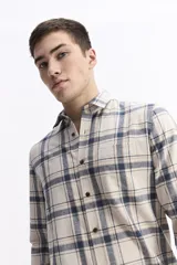 Camisa de manga larga confeccionada en viyela de algodón con estampado a cuadros en tonos beige y azul. Presenta cuello clásico, cierre frontal con botones y un bolsillo aplicado en el pecho.