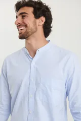 Camisa blanca de manga larga con cuello mao y bolsillo en el pecho.