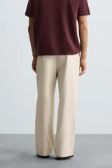 Pantalón de corte recto, color beige claro, con pliegues frontales y bolsillos de vivo en la parte trasera.