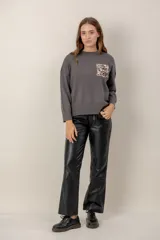 Sweater negro de punto con cuello redondo, mangas largas y un bolsillo frontal decorado con lentejuelas brillantes.