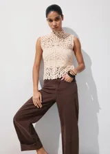 Top de tejido calado color beige, con cuello halter, sin mangas y cierre de botones en la espalda.