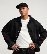 Campera masculina de jean negro con efecto desteñido, modelo boxy, con cuello solapa, manga larga con puño abotonado, cierre frontal con botones, bolsillos grandes y recortes.