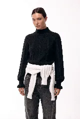 Polera de cuello alto con diseño de trenzas verticales en el tejido, mangas largas con puños acampanados y ajuste holgado.