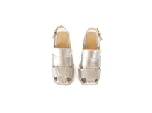 Sandalias de cuero plateado con tiras anchas entrecruzadas, punta cuadrada, talón descubierto con tira ajustable y hebilla metálica, y taco ancho de altura media.