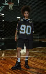 Camiseta estilo jersey de fútbol americano, color negro, con cuello en V ribeteado en blanco y dorado. Presenta el número "90" grande en el frente con borde blanco y dorado. Tiene inscripciones bordadas en el pecho como "L.A." y "Ravers", y el número "9" en la manga.