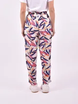 Pantalón babucha de tiro alto con cintura fruncida y lazo para ajustar. Estampado de hojas tropicales en tonos naranja y marrón sobre fondo blanco.