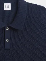 Buzo de punto acanalado color azul marino, con cuello polo y cierre frontal de dos botones. Presenta puños y ruedo elásticos.