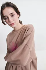 Buzo de felpa color marrón con estampa frontal en rosa, cuello redondo y hombros caídos.