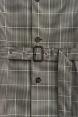 Trench de corte relajado con estampado de cuadros en tonos beige y marrón, cuello solapa en piel marrón, manga larga, bolsillos de vivo en cadera, cinturón ajustable y cierre frontal con botones.