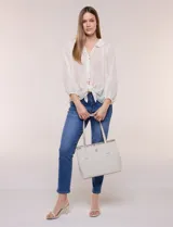 Cartera tipo tote de diseño semi-rígido y color beige, confeccionada en eco cuero. Cuenta con doble manija de hombro, base reforzada con remaches metálicos y aplique dorado con el logo de la marca en el frente.