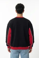 Buzo de corte oversize con diseño colorblock en negro y rojo. Presenta cuello redondo, puños y cintura acanalados, y paneles laterales con vivos blancos. Incluye logo bordado en el pecho.