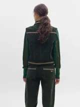 Chaleco de pana negro con cierre frontal de botones metálicos dorados. Presenta detalles de costuras en contraste en el cuello, cartera y canesú, e incluye un pequeño parche con forma de bandera en el pecho.