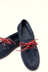 Mocasín tipo boat shoe color marrón, confeccionado en cuero, con cordones de cuero marrón y cordones decorativos azules.