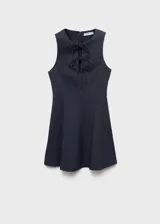 Vestido corto sin mangas de efecto denim en color azul marino, con cuello redondo y tirantes anchos. Presenta detalles de lazos en la parte delantera y diseño de tablas en la falda.
