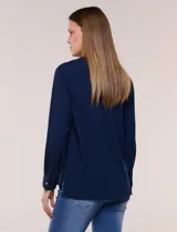Camisa blanca de corte clásico y caída fluida, con cuello camisero tradicional, abotonadura frontal oculta y mangas largas con puños anchos.