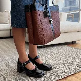 Zapato estilo Mary Jane de cuero vacuno con acabado brillante, punta cuadrada y taco bloque. Cuenta con una tira ajustable sobre el empeine con hebilla metálica.