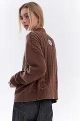 Cardigan de tejido de punto color marrón, con cuello solapa, cierre frontal de cremallera y diseño de trenzas. Cuenta con puños y dobladillo en rib elástico y un pequeño bordado en el pecho.