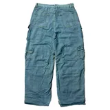 Pantalón tipo cargo de jean en color azul medio, con corte baggy fit y tiro bajo. Presenta múltiples bolsillos laterales con solapa y cierre de botón, además de un diseño holgado con frunces en la parte inferior de las piernas.