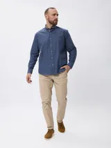 Camisa de manga larga en algodón tramado, con cuello clásico abotonado y cierre frontal con botones. Presenta un diseño liso con textura visible y un pequeño bordado en la pechera.