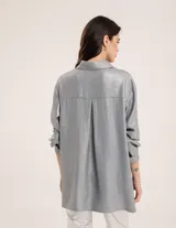 Camisa oversized con terminación metalizada color gris plomo. Tiene botones a tono en el delantero, largo por debajo de la cadera y tajos a los costados.
