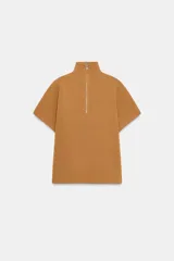 Jersey de punto color camel, de corte amplio estilo capa, con cuello alto y cremallera frontal. Presenta mangas cortas.