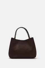 Bolso de mano de formato saca, confeccionado en material tipo gamuza color marrón oscuro, con asa superior trenzada en color negro.