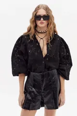 Camisa negra de encaje de algodón con cuello camisero clásico, mangas largas abullonadas con puños elásticos y cierre frontal con botones de nácar.