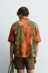 Camisa de corte relajado confeccionada en tejido fluido con mezcla de viscosa y lino. Presenta cuello bowling, manga corta y cierre frontal con botones. Diseño con estampado floral en tonos verdes y naranjas.