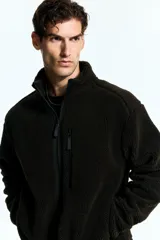 Campera deportiva de sherpa con cuello elevado, cierre frontal completo, mangas raglán, un bolsillo superior con cierre y dos bolsillos laterales. Presenta terminaciones elásticas en puños y ruedo.