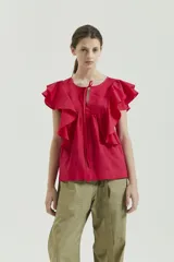 Top de voile liso color fucsia, sin mangas, con escote redondo y tajo pequeño en el centro. Tiene detalle de alforzas finas a cada lado del tajo y dos volados superpuestos que continúan de adelante hacia atrás.