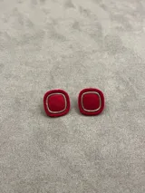 Aros de diseño cuadrado con bordes redondeados, recubiertos en terciopelo rojo con un marco metálico dorado en el centro.
