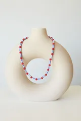 Collar tipo choker de 35 cm con 5 cm de extensión, compuesto por cuentas rojas redondas y cuentas cilíndricas blancas con franjas azules.