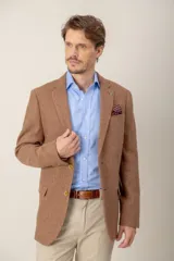 Saco de vestir color tostado con textura jaspeada, confeccionado en mezcla de lana y seda. Presenta solapas clásicas, cierre frontal de dos botones, bolsillos laterales con solapa y un bolsillo superior con pañuelo decorativo.