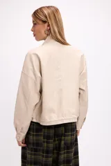 Campera corta de cuero sintético en color beige, con diseño de calce relajado, cierre frontal metálico, bolsillos con solapa en el frente y cordón ajustable en el ruedo.