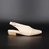 Zapato de cuero color crema, con punta fina, escote en V y laterales calados. Tiene talón descubierto, taco bajo foliado y suela de goma antideslizante.