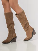 Bota de caña alta confeccionada en cuero descarne color habano, con taco cuadrado y punta redondeada.