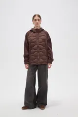 Campera con capucha de diseño híbrido, combinando un panel frontal acolchado con diseño ondulado y mangas de tejido liso. Cuenta con cierre frontal completo, puños elásticos y bolsillos laterales.