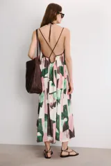 Vestido midi de corte holgado con cuello halter ajustable mediante lazada y hombros descubiertos. Presenta un diseño con tiras cruzadas en la espalda y un estampado abstracto en tonos rosado, verde y marrón sobre fondo blanco.