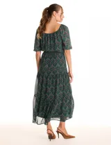 Vestido midi de gasa estampada en tonos verdes y marrones, con escote en V cruzado en la parte delantera y escote redondo elastizado en la espalda. Presenta cintura elastizada con lazo fino para anudar, mangas cortas evasé con volumen y falda con volados escalonados. Incluye forro interno a tono.